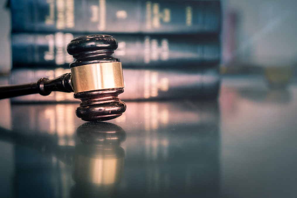 A judge's gavel resting on a reflective surface with law books in the background.